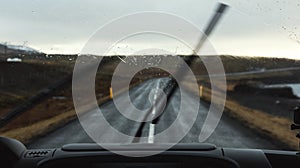 On the road in rainy day, car windshield with wipers cleaning rain drops