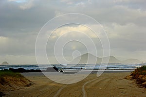 Road reaching the beach. Early morning light, with blue water and foggy sea.