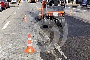 Road red cones enclose a section of the road and a road roller on a city street