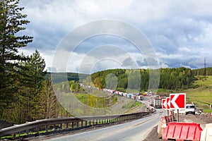 Road repair, bypass red sign, traffic on one lane, traffic jam, green forest and cloudy sky background