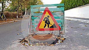 Road repair. Sewer manhole on the roadway. Triangular warning car drivers sign with a man with a yellow spade with red. Men at