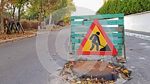 Road repair. Sewer manhole on the roadway. Triangular warning car drivers sign with a man with a yellow spade with red. Men at