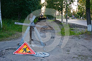 Road repair work - a yellow tractor stands on the sidewalk, which will repair. In the foreground is an anti-tank hedgehog and a