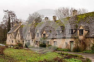 Road running alongside a row of historic quintessential Cotswold cottages in Bibury, England