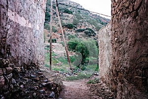 a road running between two stone buildings in a village surrounded by mountains and ruins in Morocco