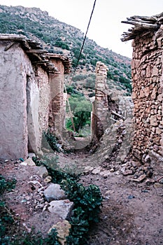a road running between two stone buildings in a village surrounded by mountains and ruins in Morocco