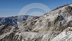 The road runs along a steep rocky snow-covered mountain slope