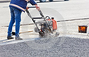 A road service worker repairs the roadway by compacting the asphalt with a plate petrol vibrator