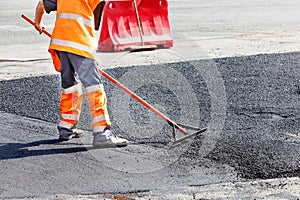 A road service worker smooths hot asphalt with a metal level manually when repairing a road