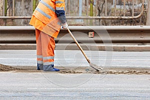 A road service worker uses a shovel to scrape off accumulated sand and debris between the lanes of the road