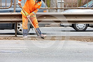 A road service worker woman uses a shovel to scrape off accumulated sand and debris between the lanes of the road