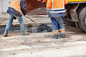 Road service workers level fresh asphalt with a shovel for patching the road