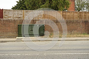 Road side green telecoms cabinet in front of brick wall & fence in Great Blakenham.