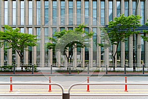 Road side view in front of a building with glass windows. A blocking fence is installed between the road and the sidewalk, making