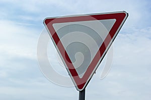 Road sign against the sky. White triangle with red border. Signal, Give way. Summer day