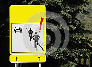 Road sign: attention to cyclists, with the silhouettes of two cyclists and a car that arrives in the opposite direction.