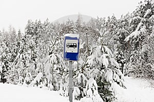 Road sign bus stop in winter in a distant village and snow covered pine trees with cloudy sky