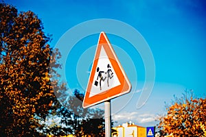 Road sign caution children over blue sky background and tree