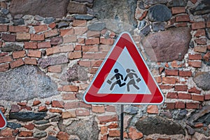 Road sign caution children over stone wall background.