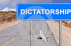 Road sign. Dictatorship location mark. The word is written on a blue signboard located opposite the old empty road with broken tra