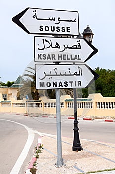 Road sign with directions to Monastir, Sousse and Ksar Hellal is in town of Tunisia. English and Arabic inscriptions. Africa