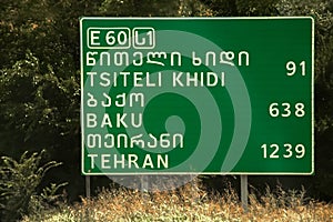 Road sign with distances to Baku and Tehran and Tsiteli Khidi in multiple scripts - Near Tbilisi Georgia