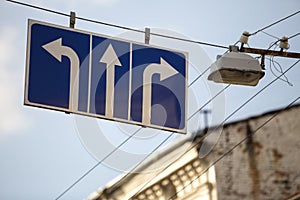 Road sign high over street with three white arrows on blue background showing direction.