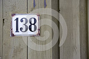 Road sign on a house reading the number 138 made out of brown ceramic.