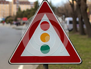 A road sign that indicates a traffic light intersection with a blurred background