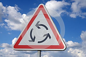 Road sign indicating a roundabout in close-up on the background of the sky with clouds