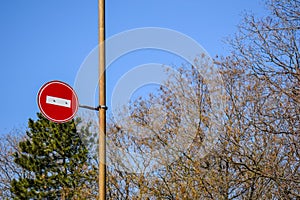 Road sign No entry against the blue sky and trees