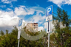 Road sign Parking space for the disabled in a residential area against the background of the sky and green trees. Capital letter P