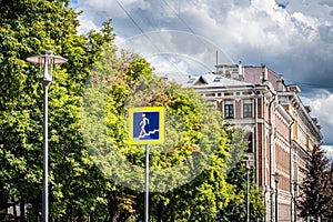 Road sign pedestrian underpass on the background of the cityscape. Street lights, yellow-green leaves of trees and thunderstorm