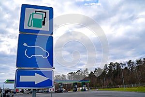 Road sign, pointed out to power station, with usual kinds of fuel and electric vehicle charging station EV, on blue background