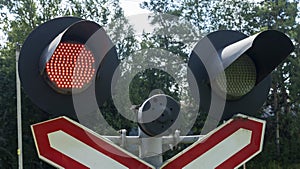 Road sign of railway crossing with double traffic light, shining red indicating approaching train