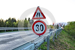 Road sign, reduce speed to 30, blurred red traffic light and con