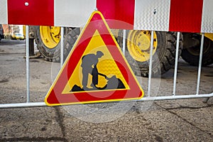 Road sign in repair. road section in repair. against the background of a large excavator, tractor or backhoe.