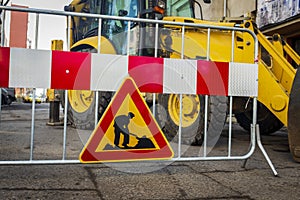 Road sign in repair. road section in repair. against the background of a large excavator, tractor or backhoe.