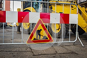 Road sign in repair. road section in repair. against the background of a large excavator, tractor or backhoe.