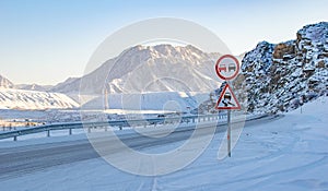 Road sign on a slippery road against the background of a winter mountain landscape