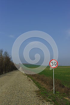 Road sign speed limit traffic 30 miles per hour standing on the side of the dirt road along the fields of green shoots