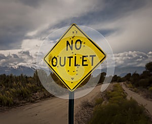 A road sign stating No Outlet riddled with bullet holes