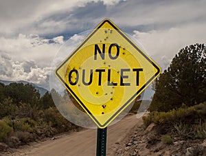 A road sign stating No Outlet riddled with bullet holes in the country