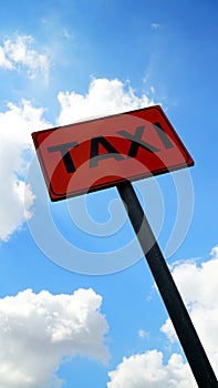 Road sign with TAXI written on an orange background with blue sky with clouds in the background