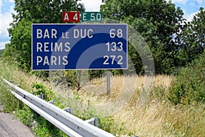 A road sign to the towns of Bar le Duc, Reims and Paris, 272 km away, on an abandoned highway among green trees and grass on the w