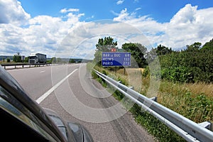 A road sign to the towns of Bar le Duc, Reims and Paris, 272 km away, on an abandoned highway among green trees and grass on the w