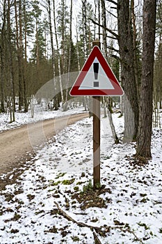 Road sign triangular shape with exclamation mark. Winter road in forest