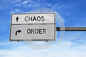 Road sign with words chaos and order. White two street signs with arrow on metal pole on blue sky background