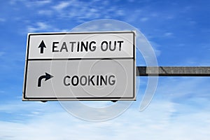 Road sign with words eating out versus cooking. White two street signs with arrow on metal pole. Directional road, Crossroads Road