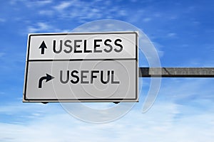 Road sign with words useless versus useful. White two street signs with arrow on metal pole on blue sky background